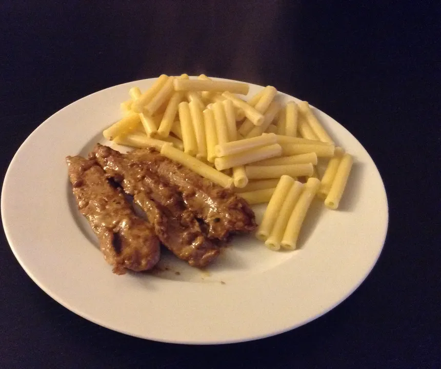 Aiguillettes de canard nappées de sauce, servies avec des macaronis